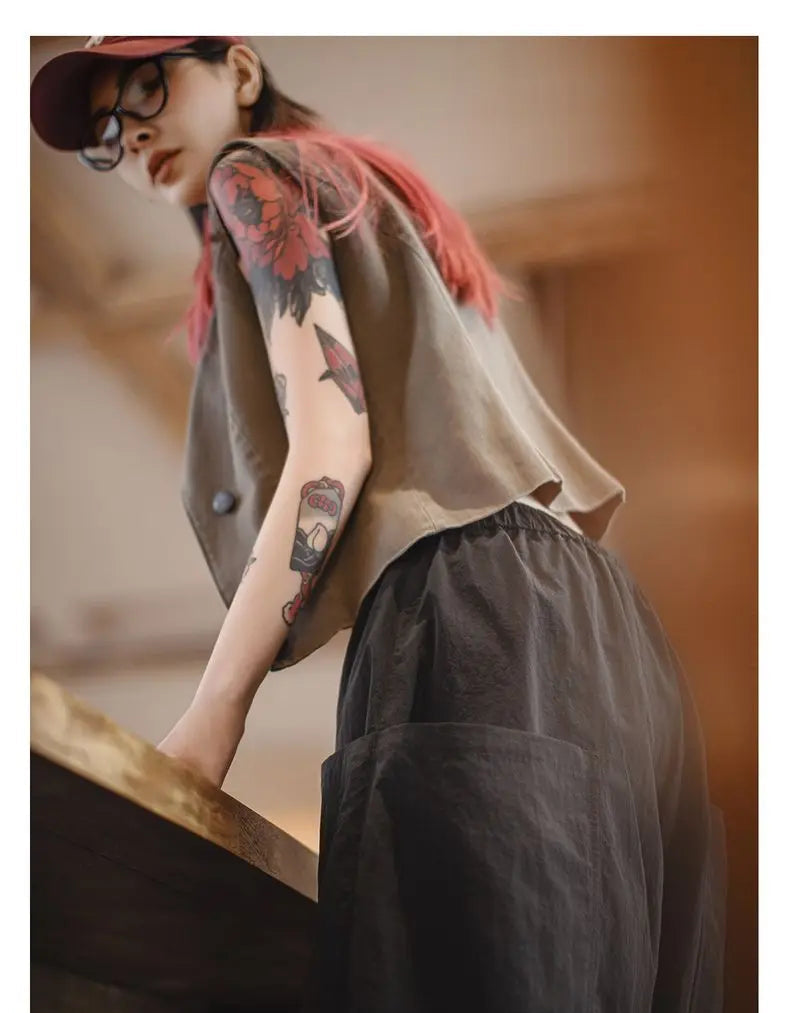 Person wearing a beige shirt and black pants with visible tattoos, sitting on a wooden bench.