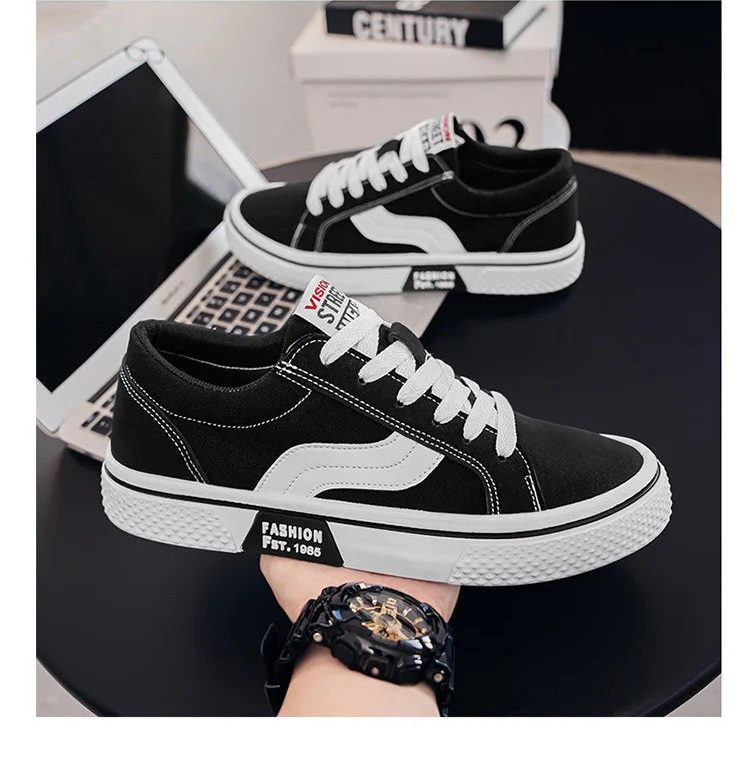 Black and white sneakers being held with a laptop and books in the background