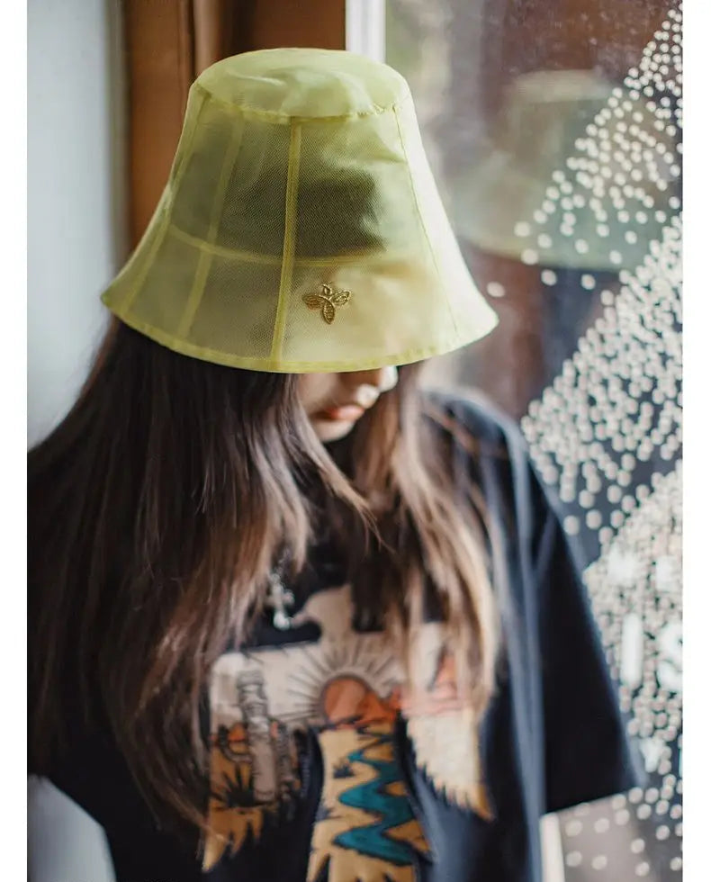 Person wearing a yellow bucket hat with a brand logo, sitting indoors.